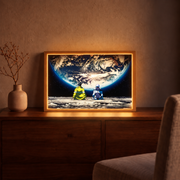 To the Moon With You glowing framed artwork displayed on a wooden cabinet in a warmly lit room.